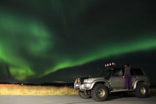 A super jeep with a woman standing on its ledge under the northern lights in Iceland.