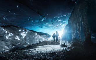 Two people stand in the entrance to an ice cave.