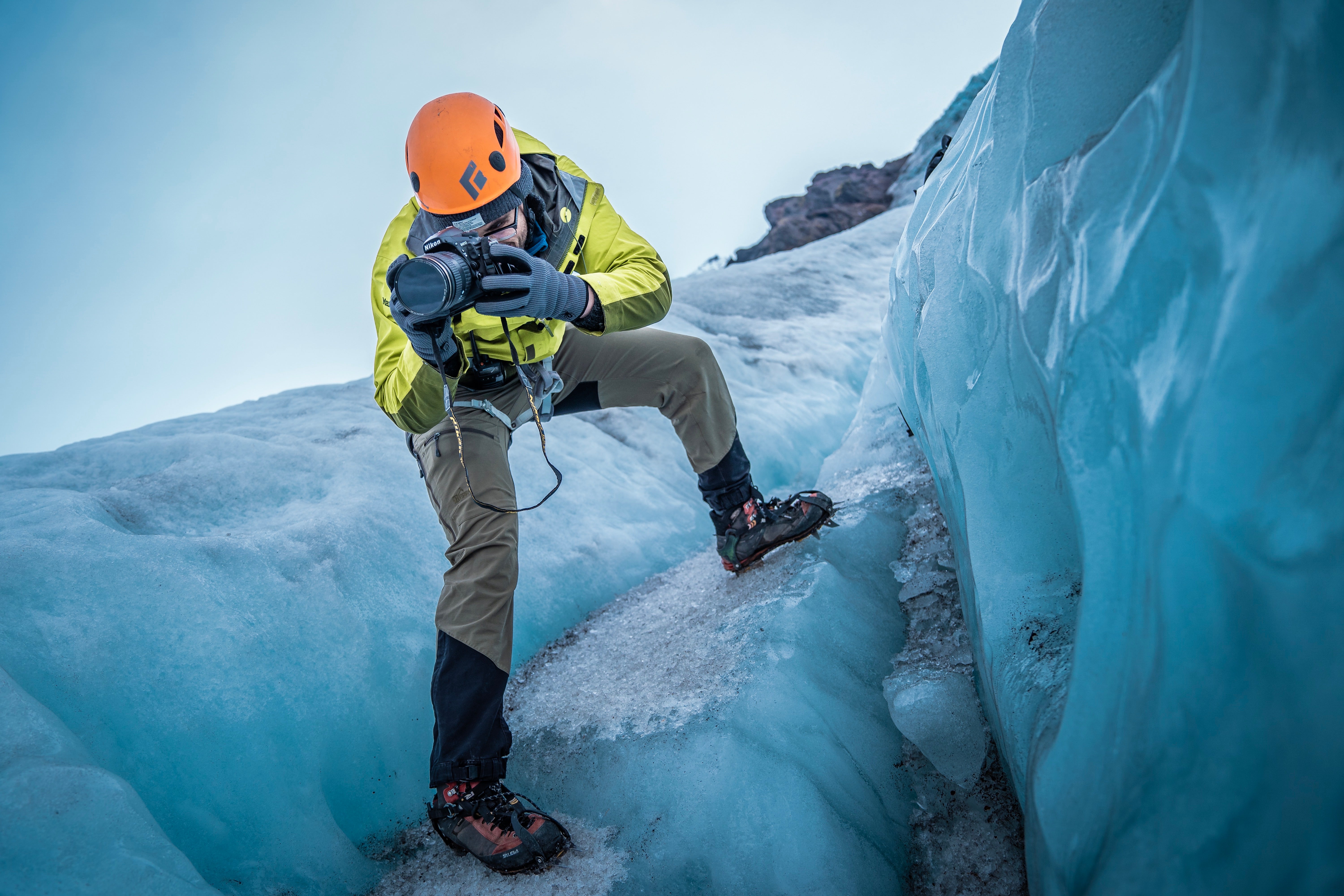 A professional photographer leans down over the edge of an ice cave in Iceland with his camera.