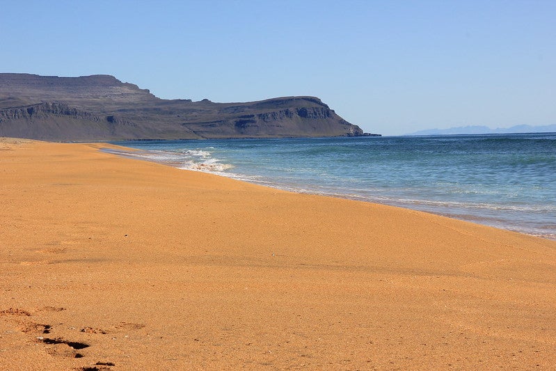 Golden sand and calm waves at Raudisandur Beach in Iceland with cliffs in the background.