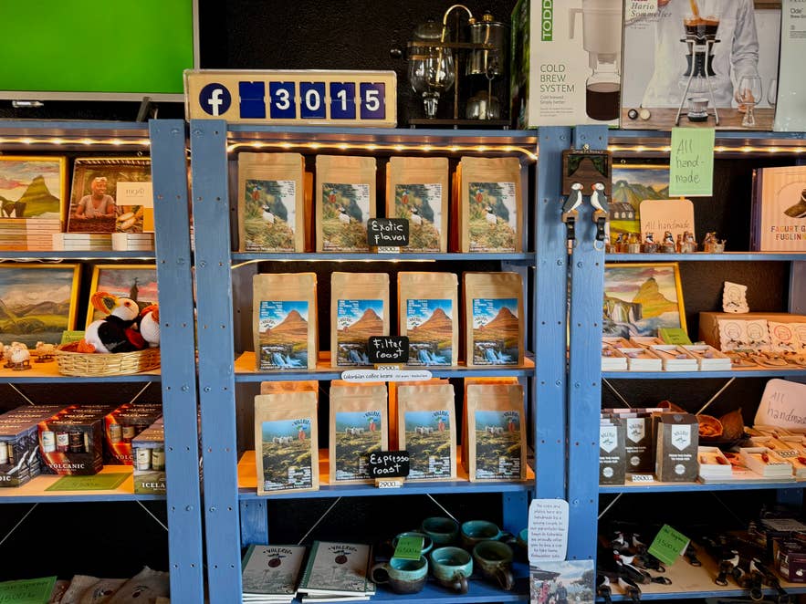 Sachets de café, souvenirs représentant des macareux, mugs et objets artisanaux faits main sur une étagère en bois bleu chez Valeria Coffee.