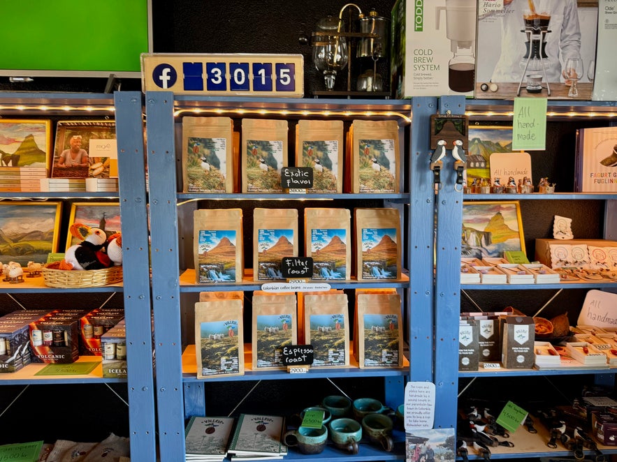 Coffee bags, puffin souvenirs, mugs, and handmade crafts on a blue wooden shelf at Valeria Coffee.