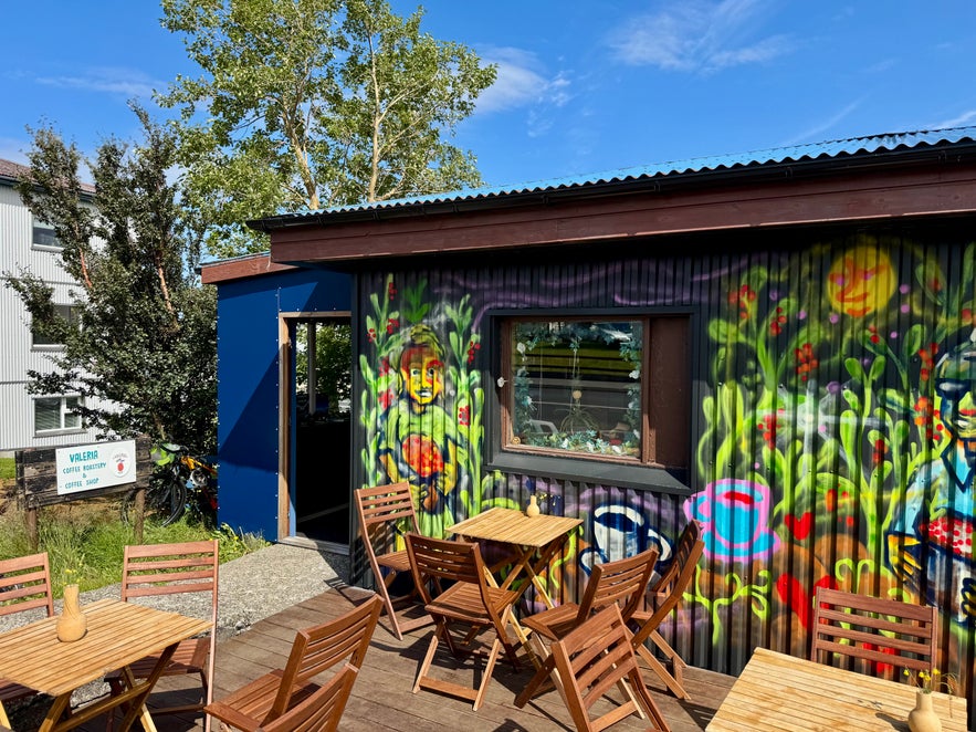Wooden patio tables and chairs outside Valeria Coffee, with mural art and potted wildflowers in small vases.