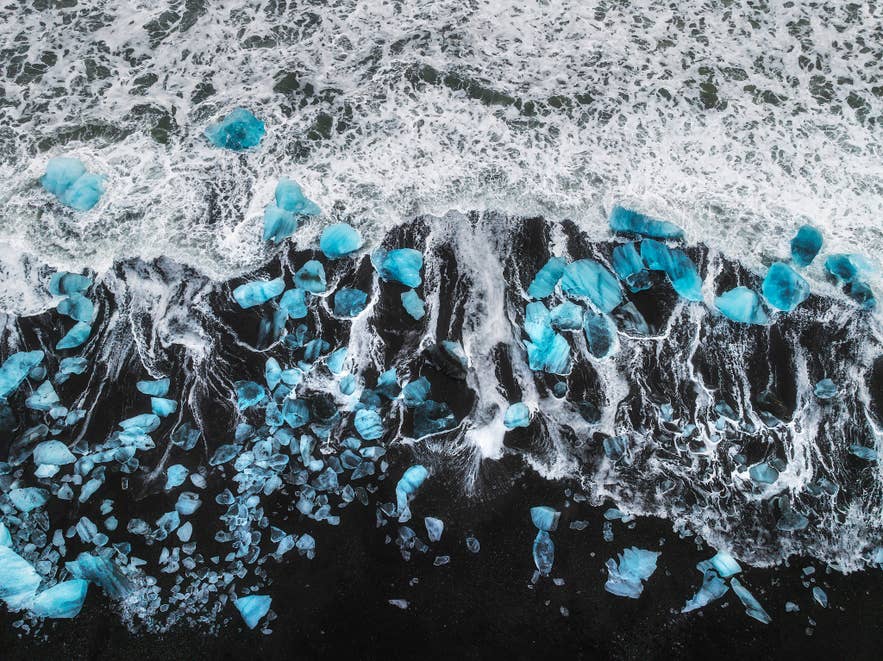 Une vue aérienne de la Plage de diamants montre des blocs de glace éparpillés, semblables à des pierres précieuses scintillantes sur le sable noir.