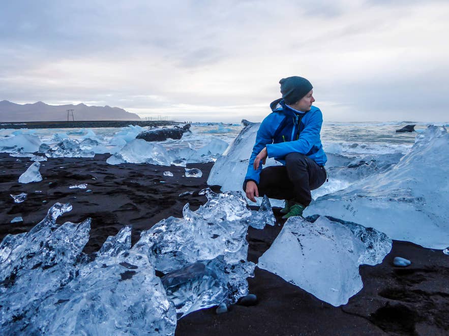 Un touriste à la Plage de diamants regarde l’océan, avec des morceaux de glace éparpillés sur le sable noir.