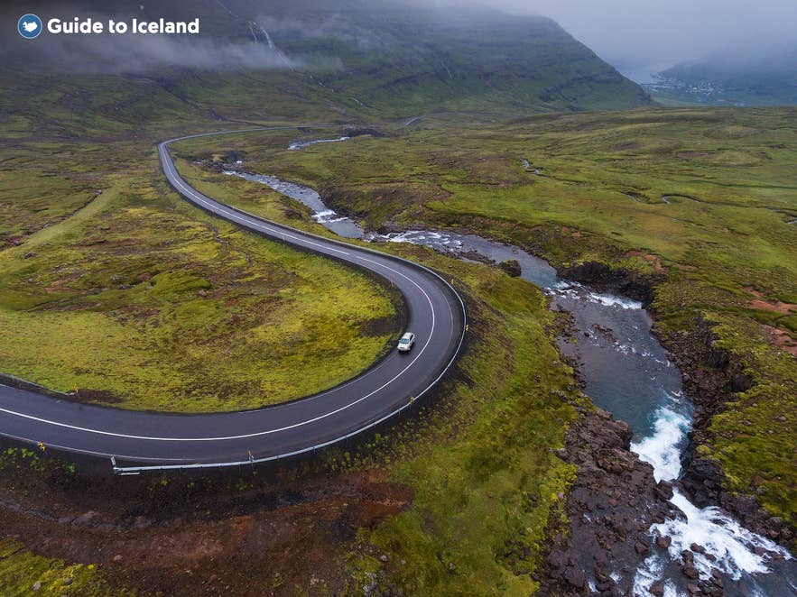 Winding mountain road near Seydisfjordur in East Iceland, with a river running alongside green mossy hills under low-hanging clouds