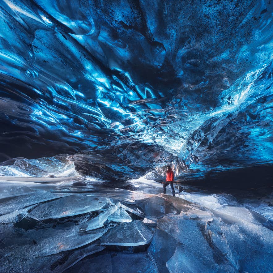 En besøkende utforsker en blå isgrotte i Vatnajökull nasjonalpark, omgitt av glatte, frosne isvegger.