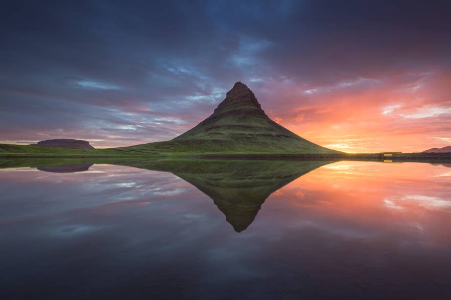 Kirkjufell is in de zomer bedekt met mos en weerspiegelt in het kalme water eronder.