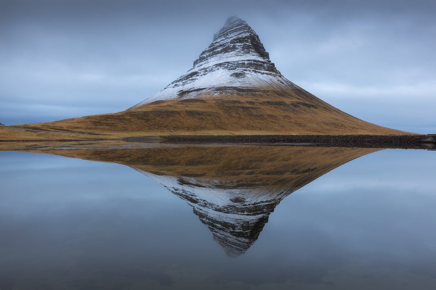 Snow-dusted Kirkjufell Mountain in early winter is reflected in the water, creating a striking mirrored image.