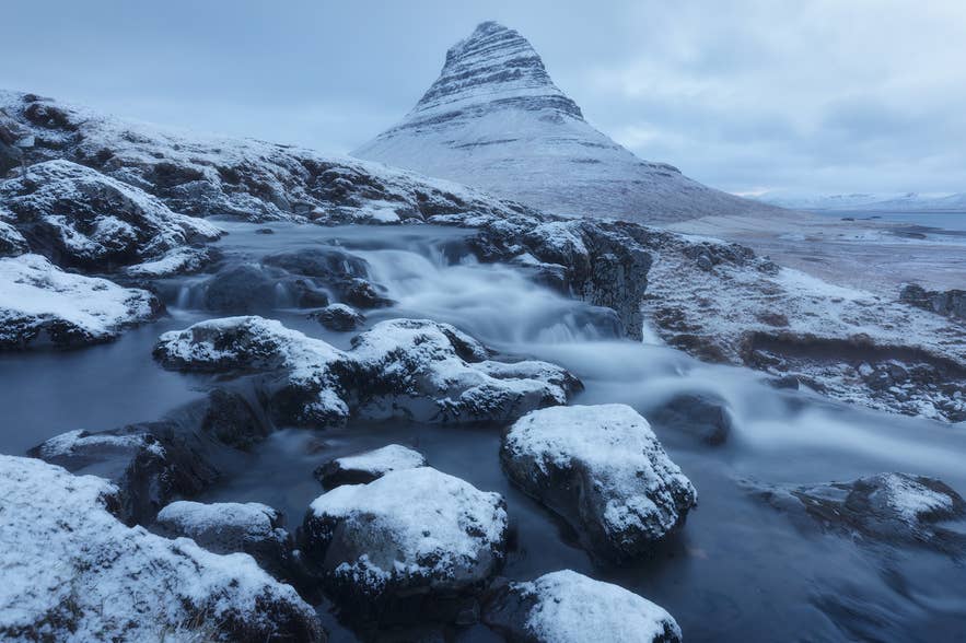 Kirkjufell in de winter met ijzige stenen op de voorgrond.