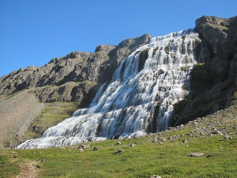 Dynjandi Waterfall cascading over rocky cliffs in the Westfjords of Iceland under a clear blue sky.