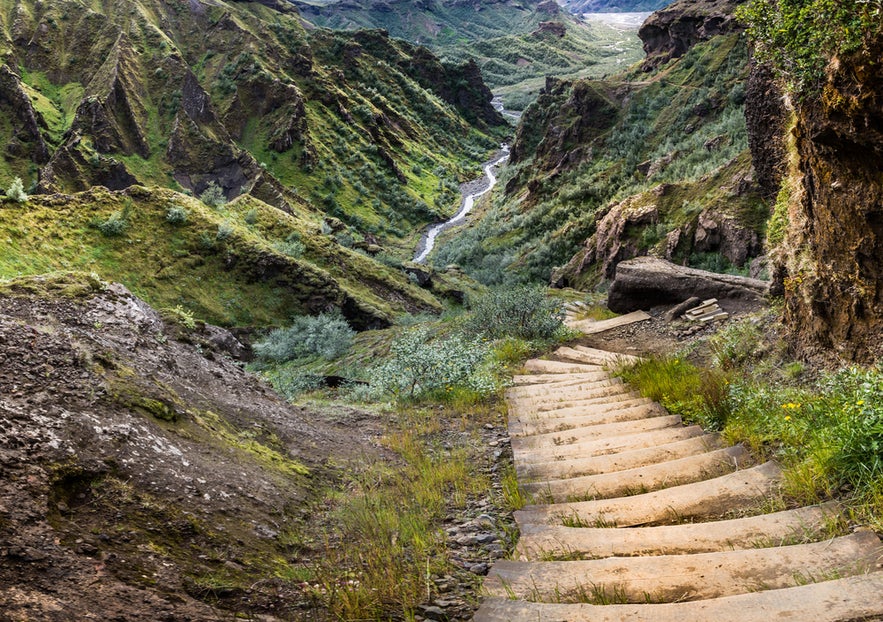 Hiking trail steps leading into Thorsmork Valley in Iceland, surrounded by lush green cliffs and a winding river.
