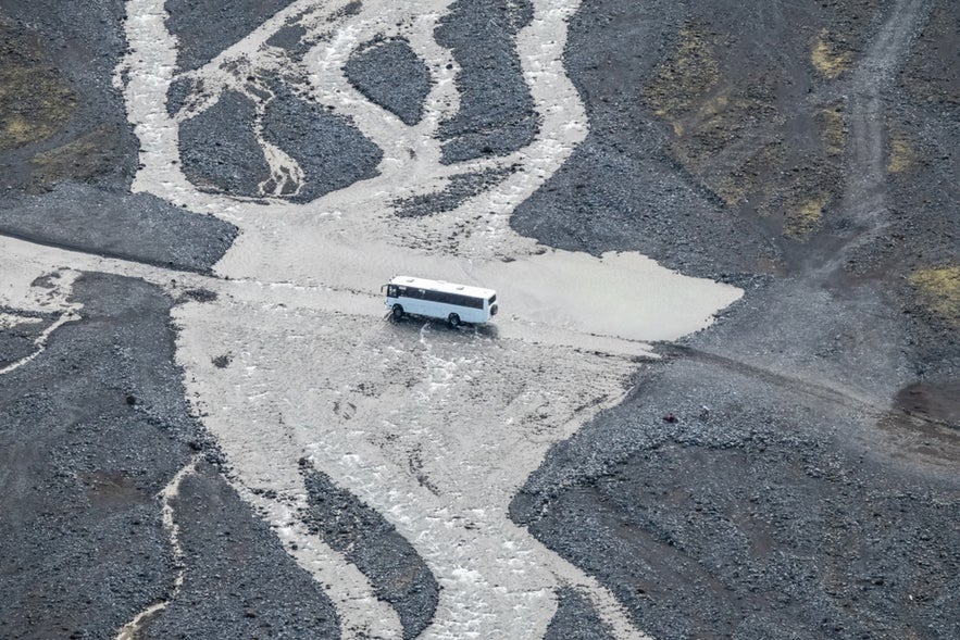 Bus crossing a glacial river near Thorsmork, Iceland, highlighting the rugged terrain and remote beauty of the Highlands.