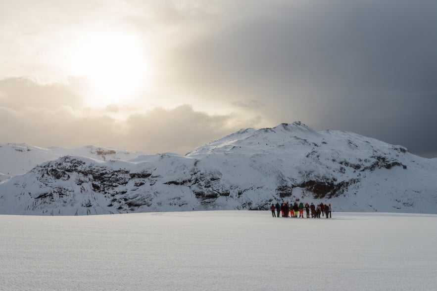 With the sun breaking through a cloudy sky, explorers walk on Eyjafjallajokull Glacier in Iceland, which can sometimes be seen from Vik.