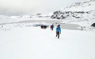 Glacier hikers ascend a snowy slope with the frozen lake and icy cliffs of Solheimajokull Glacier behind them
