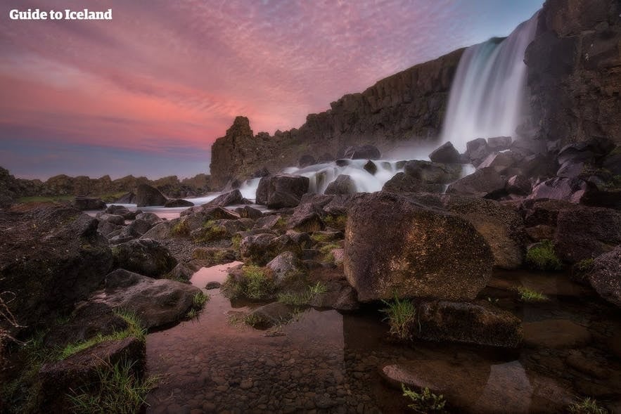 Oxararfoss waterfall at Thingvellir National Park in Iceland at sunset with dramatic rocks and pink sky