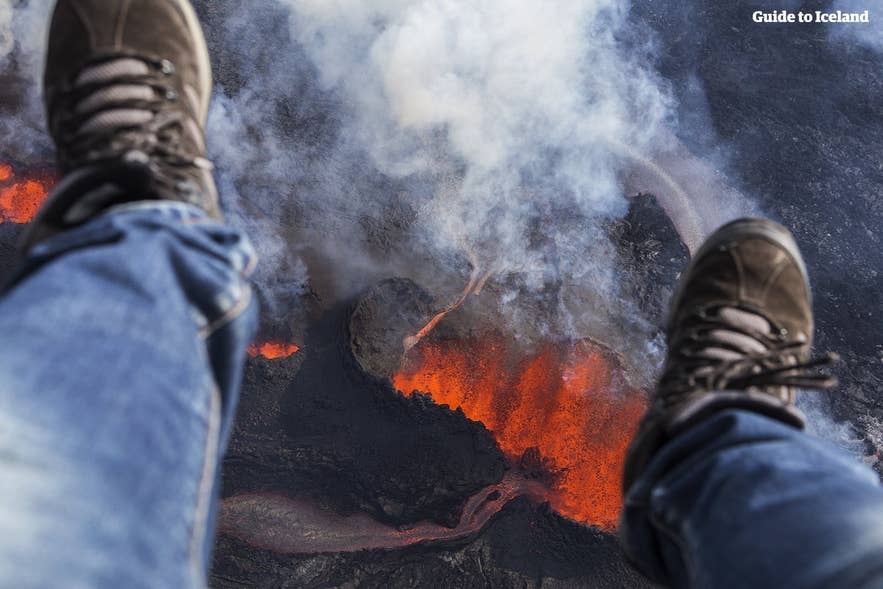 Aerial view of Icelandic volcano eruption with traveler’s legs in frame when on helicopter tour over glowing lava