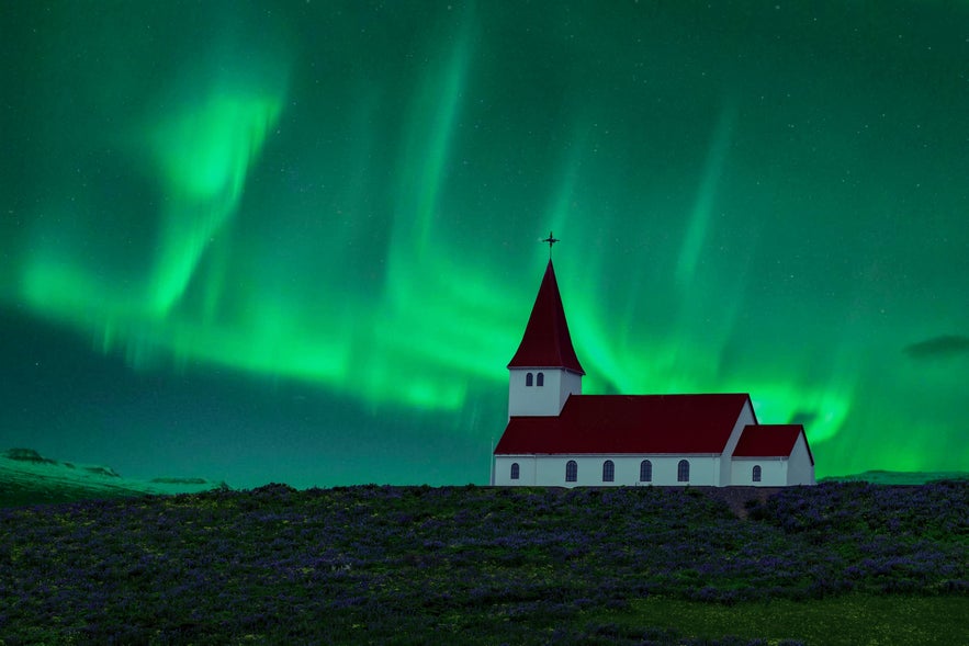 Northern lights illuminate Vik i Myrdal Church under the dark Icelandic sky.