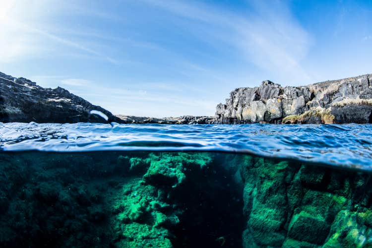 Surface view of Bjarnagja fissure showing rugged lava rocks above and green volcanic walls below the waterline.
