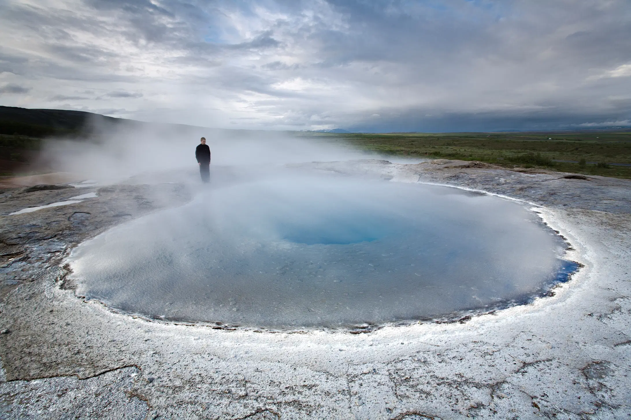 Una piscina termale geotermica fumante nell'area geotermica di Geysir in Islanda, con una persona in piedi sul bordo.