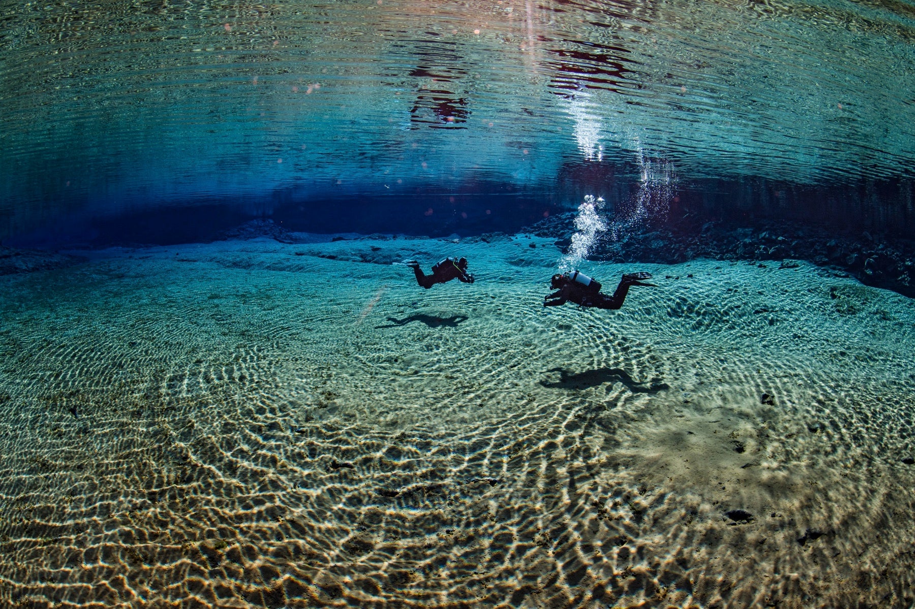 Two divers swimming in the crystal-clear waters of Silfra fissure in Iceland.