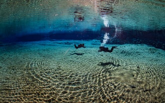 Two divers swimming in the crystal-clear waters of Silfra fissure in Iceland.