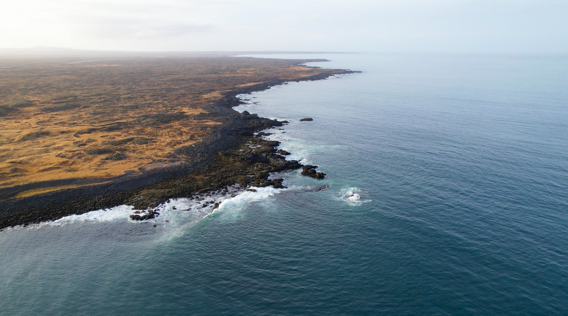 Aerial view of rugged volcanic shoreline along the Ottarsstadir coast.