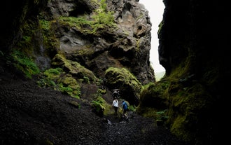 Person hiking in a narrow canyon with moss-covered black volcanic rocks in Thorsmork.
