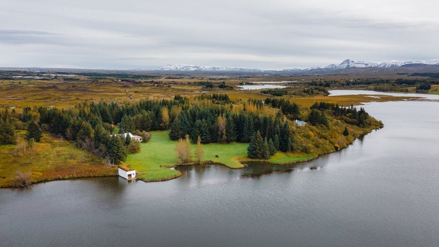 Aerial view of Lae Ellidavatn near Reykjavik, a calm lake surrounded by forest, popular for fishing and nature walks.
