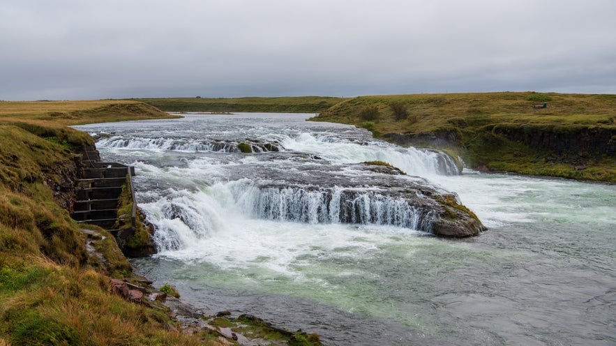 Small cascading waterfall on the West Ranga River in Iceland, with a fish ladder on the left and grassy fields.