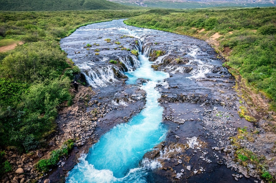 The Bruara River flows through lush greenery with clear blue water, a scenic spot popular for fishing in Iceland.