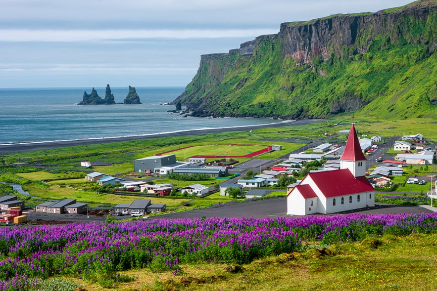 Scenic view of Vik with its red-roof church and sea stacks, a charming South Iceland town near Yoda Cave and Reynisfjara Beach.