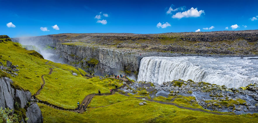 Dettifoss Waterfall in North Iceland with visitors hiking along a scenic trail beside the powerful cascade.