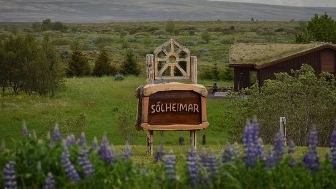 Solheimar-Ökodorf-Schild in Island, umgeben von Natur und Blumen – bekannt für nachhaltiges Leben und lokales Shopping.