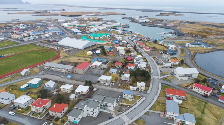 Aerial view of Hofn, Iceland, a coastal town with colorful homes, a harbor, and local shopping spots near the shoreline.