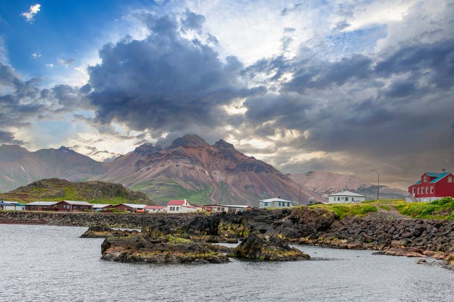 Bunte Häuser in Borgarfjördur Eystri, Ostisland, vor dramatischer Bergkulisse und bewölktem Himmel am Meer.