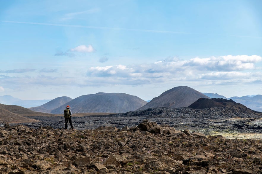 Hiker standing on rocky lava field near Sundhnukagigar volcano with volcanic hills in the distance