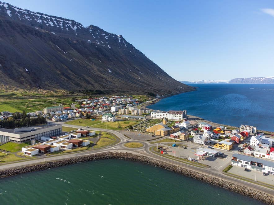 Luftfoto af Ísafjörður, en kystby i Vestfjordene, Island, med farverige huse, stejle bjerge og en rolig bugt.