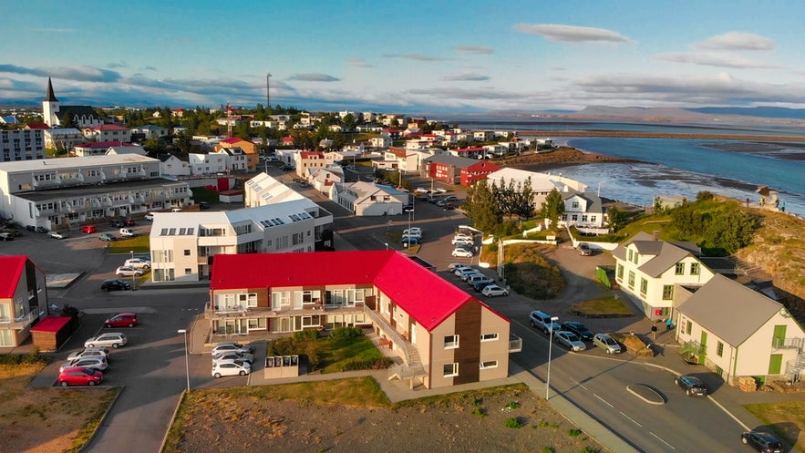 Aerial view of Borgarnes, Iceland, with red-roofed buildings, coastal scenery, and a backdrop of mountains and ocean.