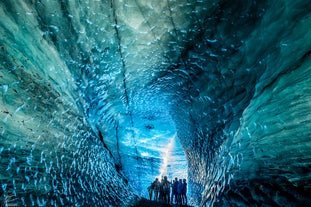 A group of people are gathered inside the blue ice cave of Katla, surrounded by beautiful blue colored ice walls.