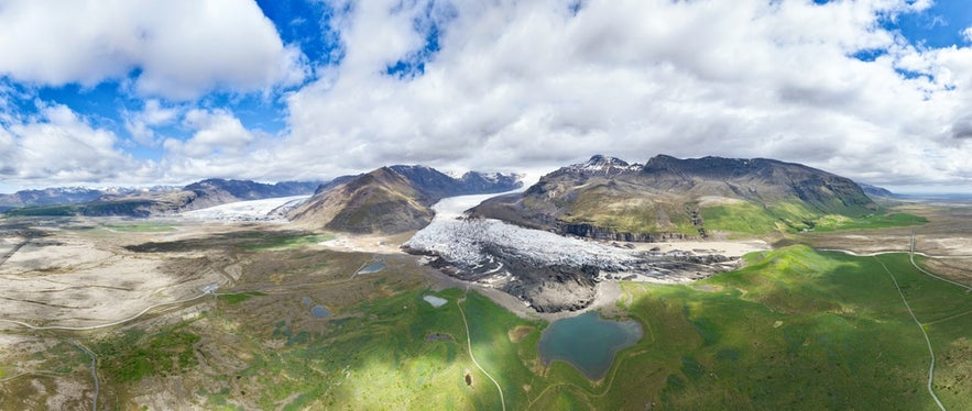 Aerial view of glacier and mountains near Svinafell, Iceland, with green fields and camping area visible in the landscape.