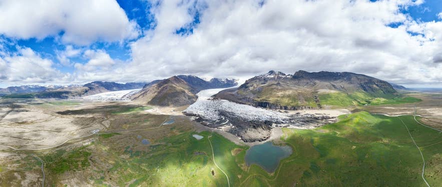 Flygbild över glaciär och berg nära Svinafell, Island, med gröna fält och campingområde i landskapet.