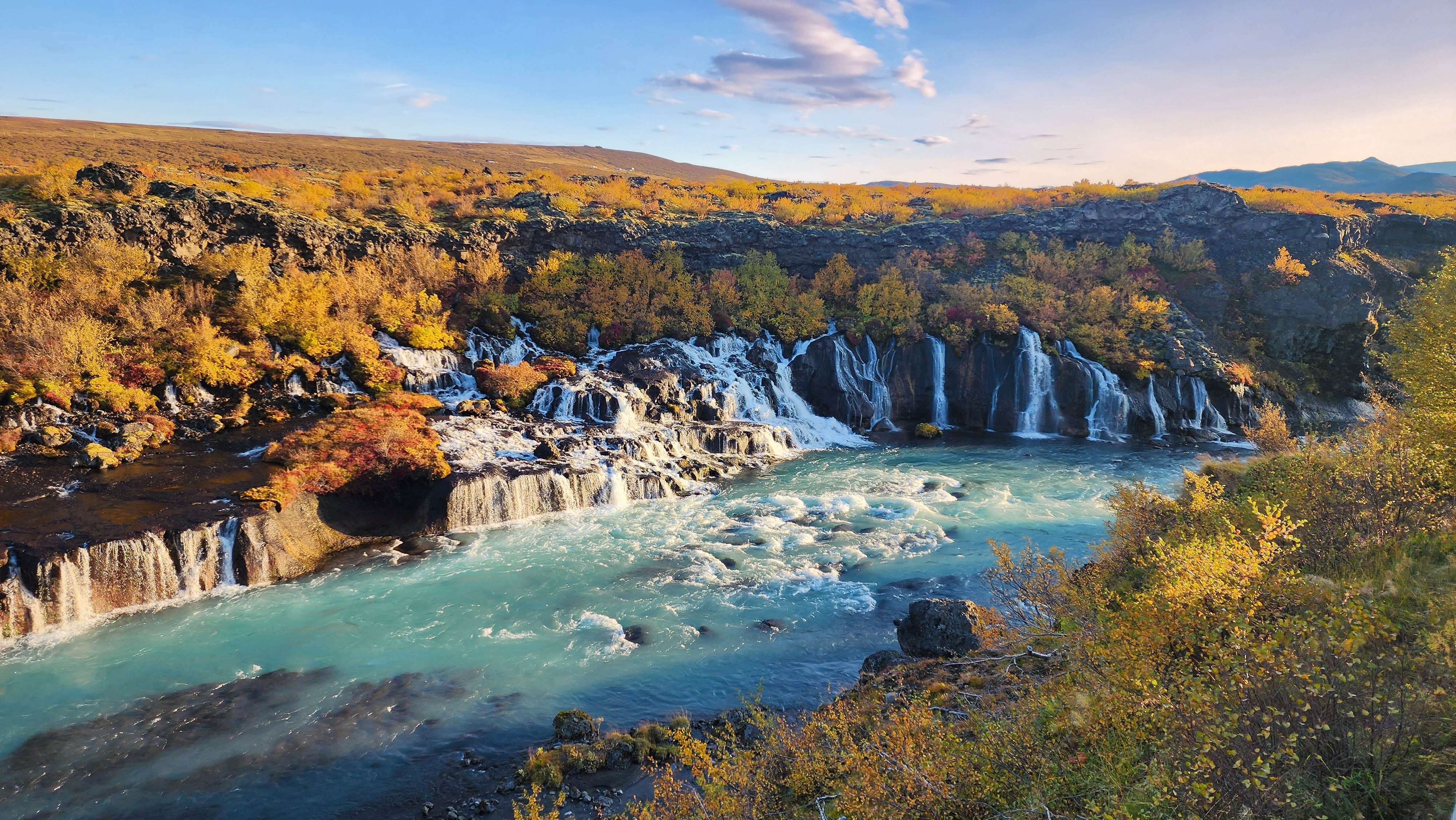 La cascata Hraunfossar scorre tra campi lavici e vegetazione autunnale.