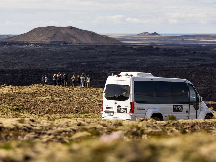Volcano shuttle van with group of tourists at Icelandic lava field near active volcanic site