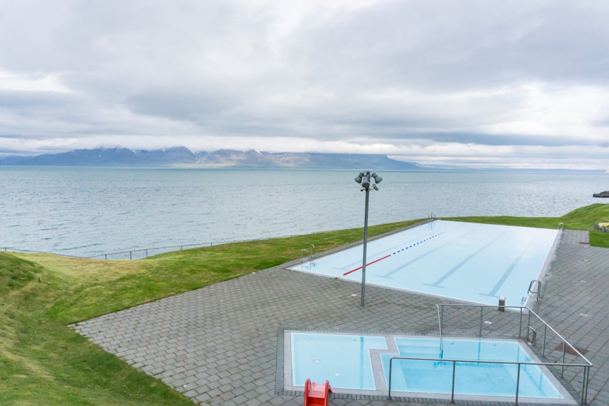 Infinity swimming pool in Hofsos, North Iceland, overlooking the fjord and distant mountains under a cloudy sky.