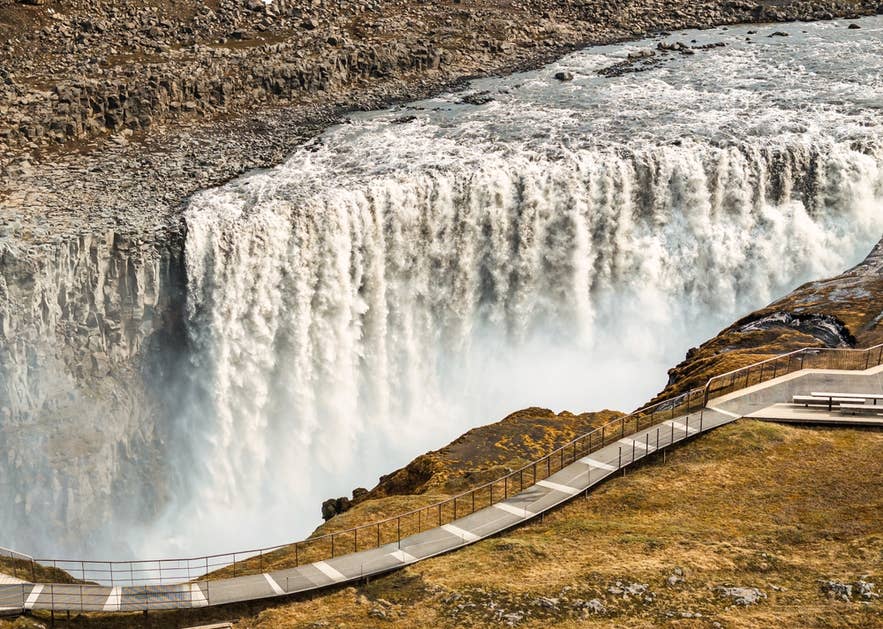 Dettifoss waterfall in Iceland, powerful water cascading over rocky cliffs with a walkway nearby.