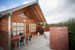 One of the terraces at Gladheimar cottages with a table and four chairs, a hot tub, and a BBQ.