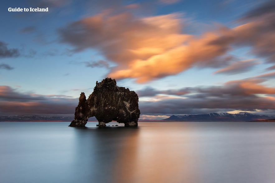 Hvitserkur rock formation off the coast of northwest Iceland at sunset, with calm waters and dramatic clouds above.