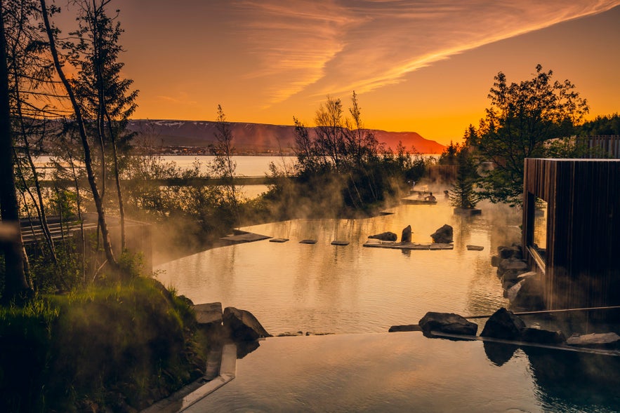 Steam rises from Iceland's Forest Lagoon under the midnight sun.