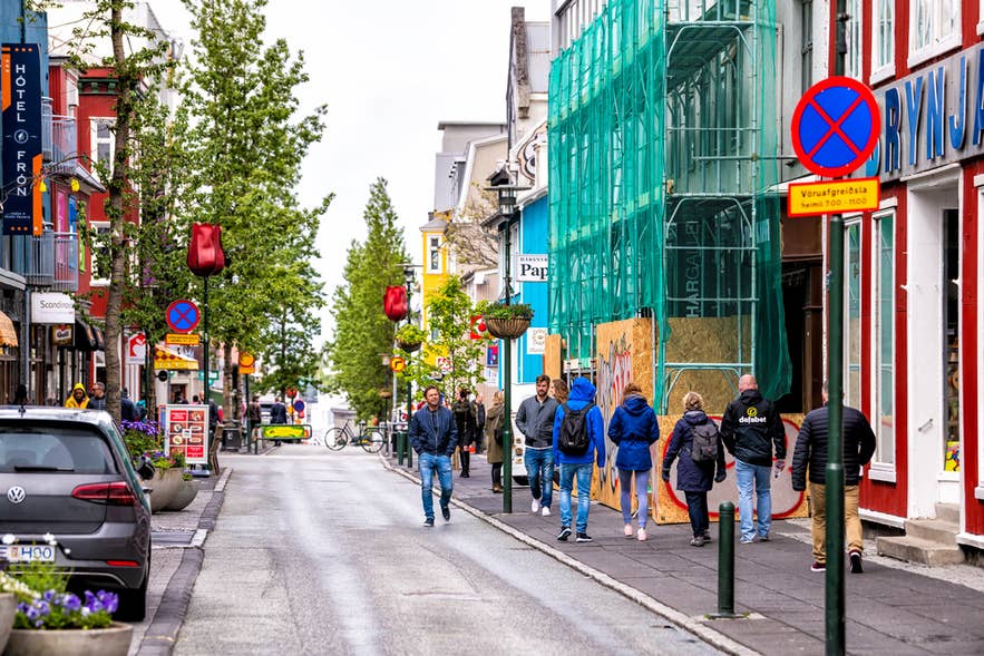 People walk along Laugavegur Street in Reykjavik, Iceland, lined with shops, signs, and colorful buildings.